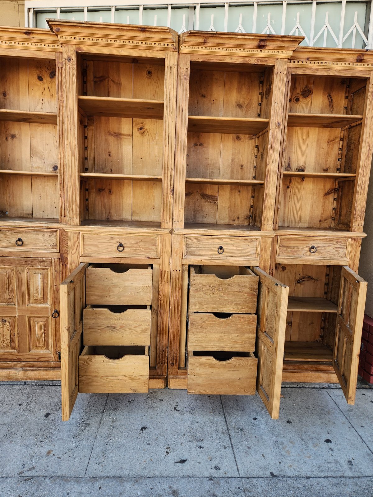 Large wooden cabinet with glass doors, shelving, and drawers displayed on a concrete surface