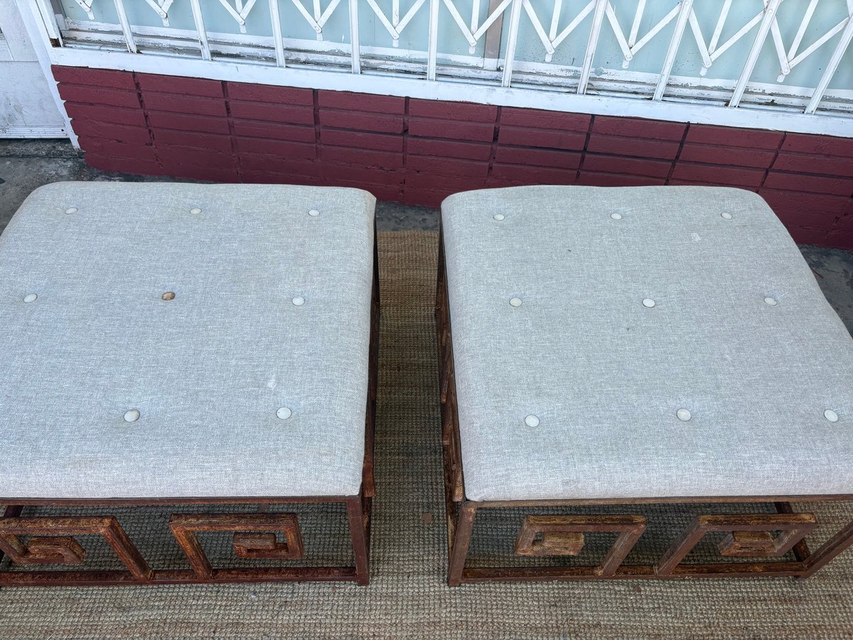 Two gray upholstered ottomans with ornate wooden bases and carved details, placed side by side on concrete