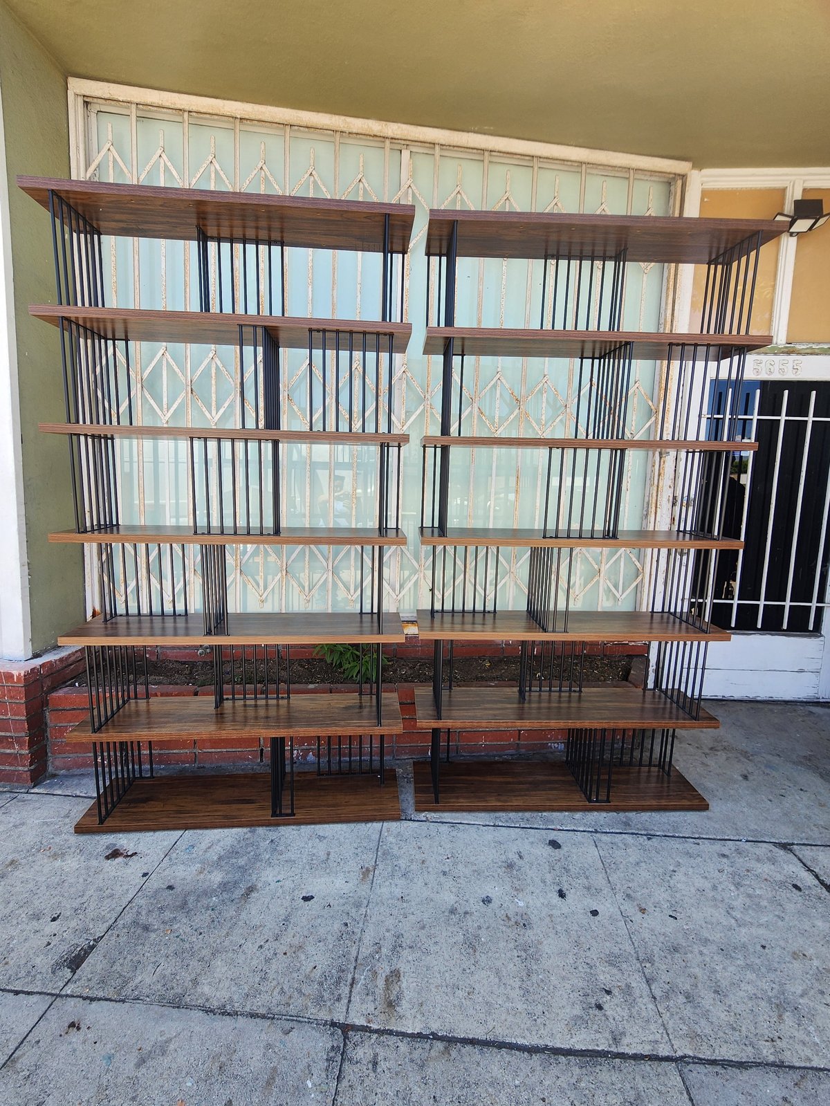 Large wooden bookshelf with metal cages or pet enclosures on a concrete driveway in front of a garage