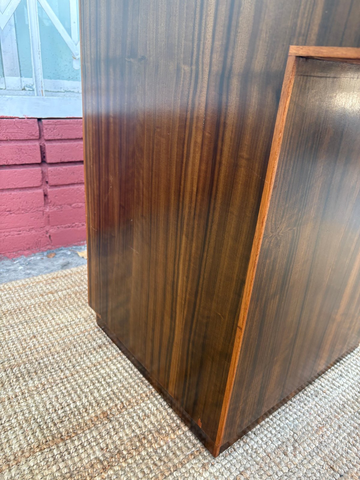 Dark wood cabinet with vertical paneling on beige carpet, with red brick wall visible in background