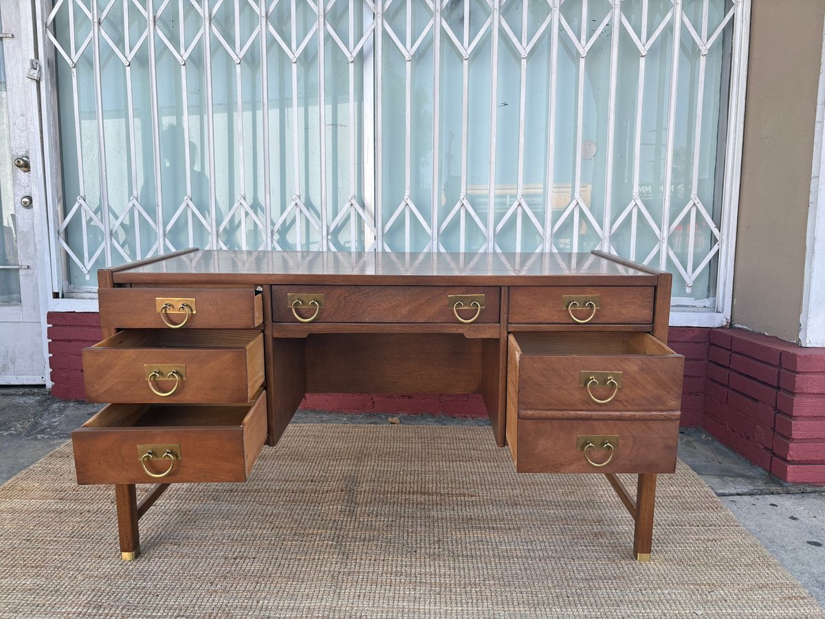 Wooden mid-century desk with six drawers and brass handles on a beige rug against an accordion door