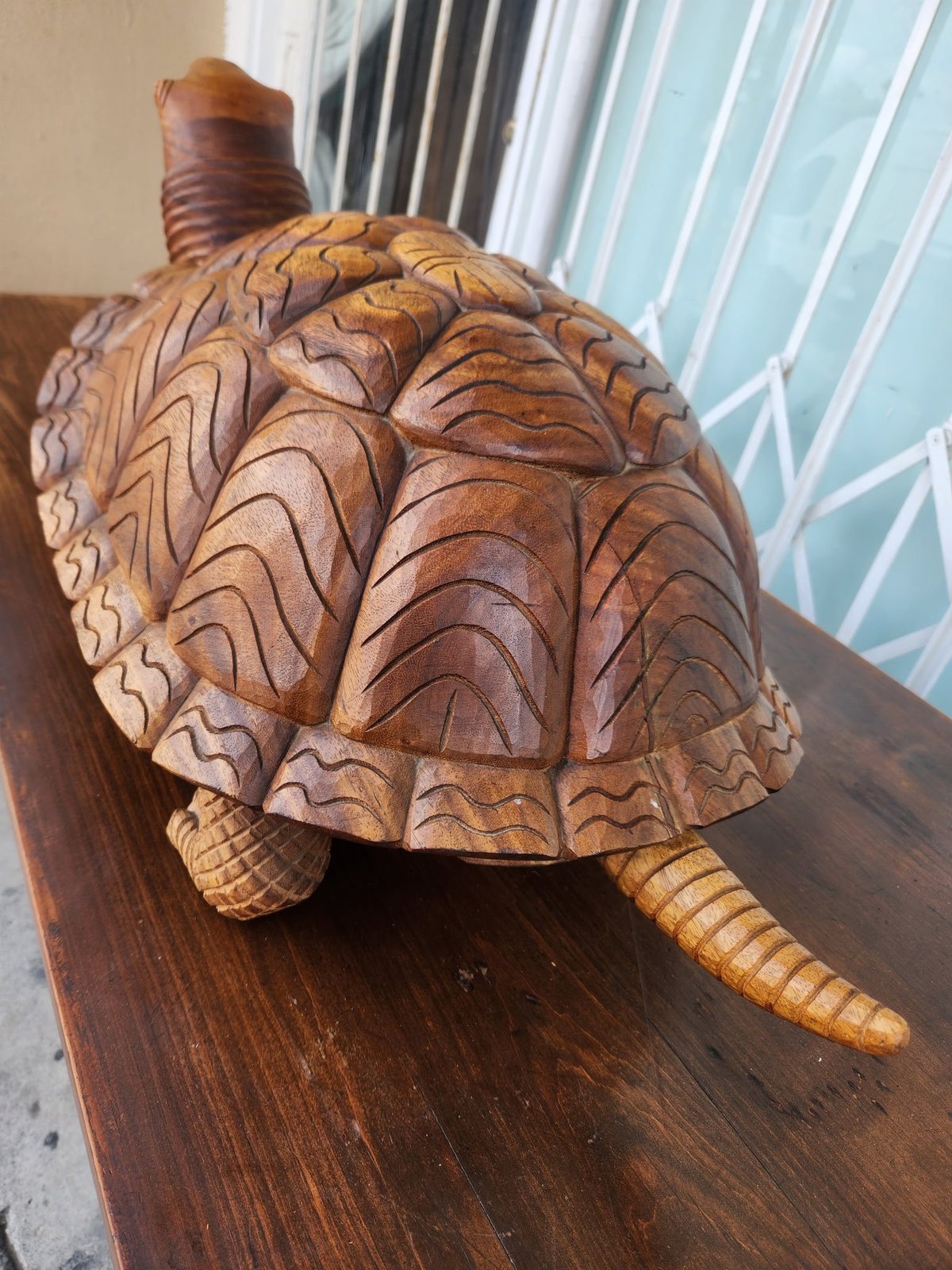 Hand-carved wooden turtle figurine with detailed shell patterns, displayed on a dark wooden base indoors