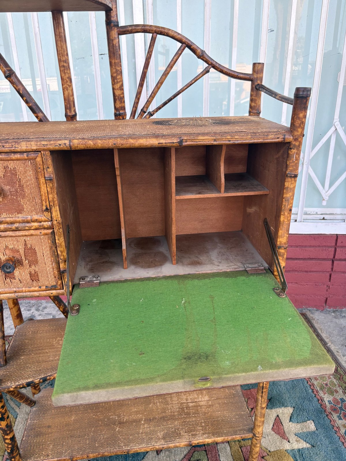 Antique wooden desk with fan-back chair, green writing surface, open compartments, and weathered finish near storefront windows