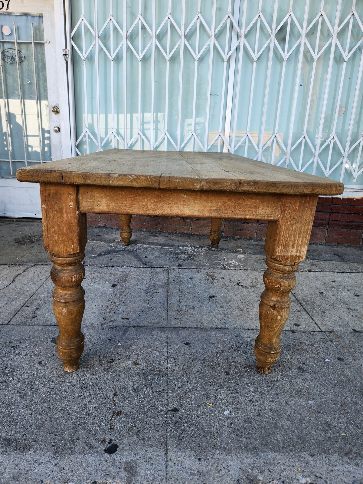 Vintage wooden table with turned legs on concrete ground in front of blue metal gate