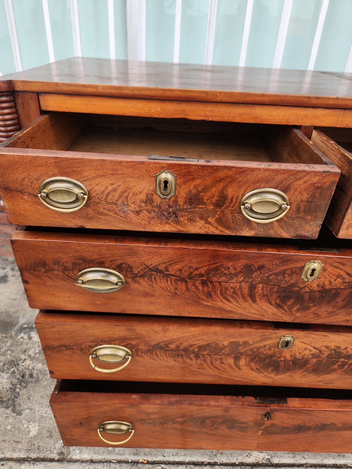 Wooden dresser with four drawers pulled open, showing brass oval handles and keyhole escutcheons on rich mahogany wood