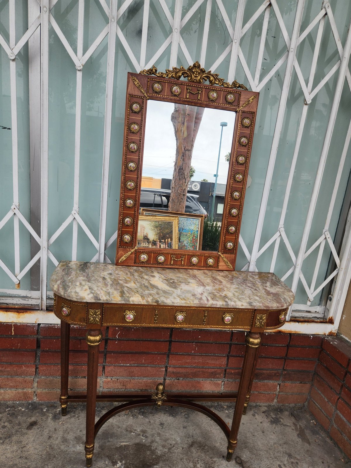 Antique wooden dresser with ornate brass-studded frame and matching mirror hanging on striped wallpaper