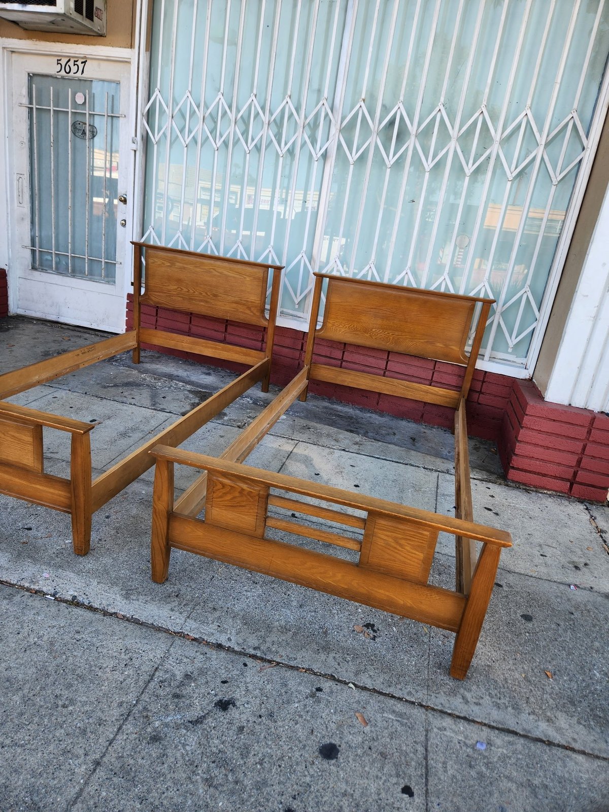 Two wooden bed frames with red/burgundy headboards displayed outside a storefront with metal gates