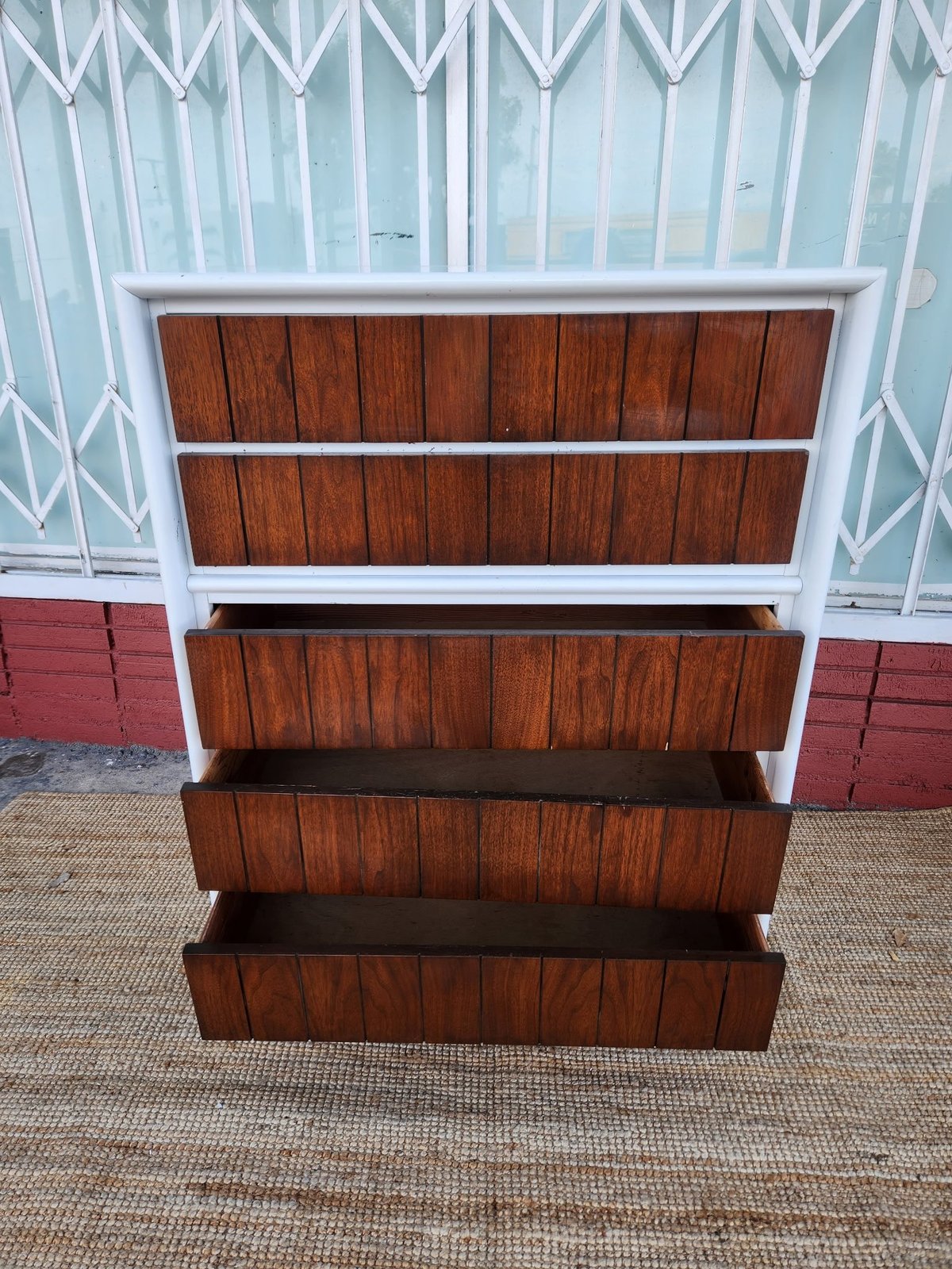Wooden dresser with five drawers and white trim frame against decorative lattice and colored panel background