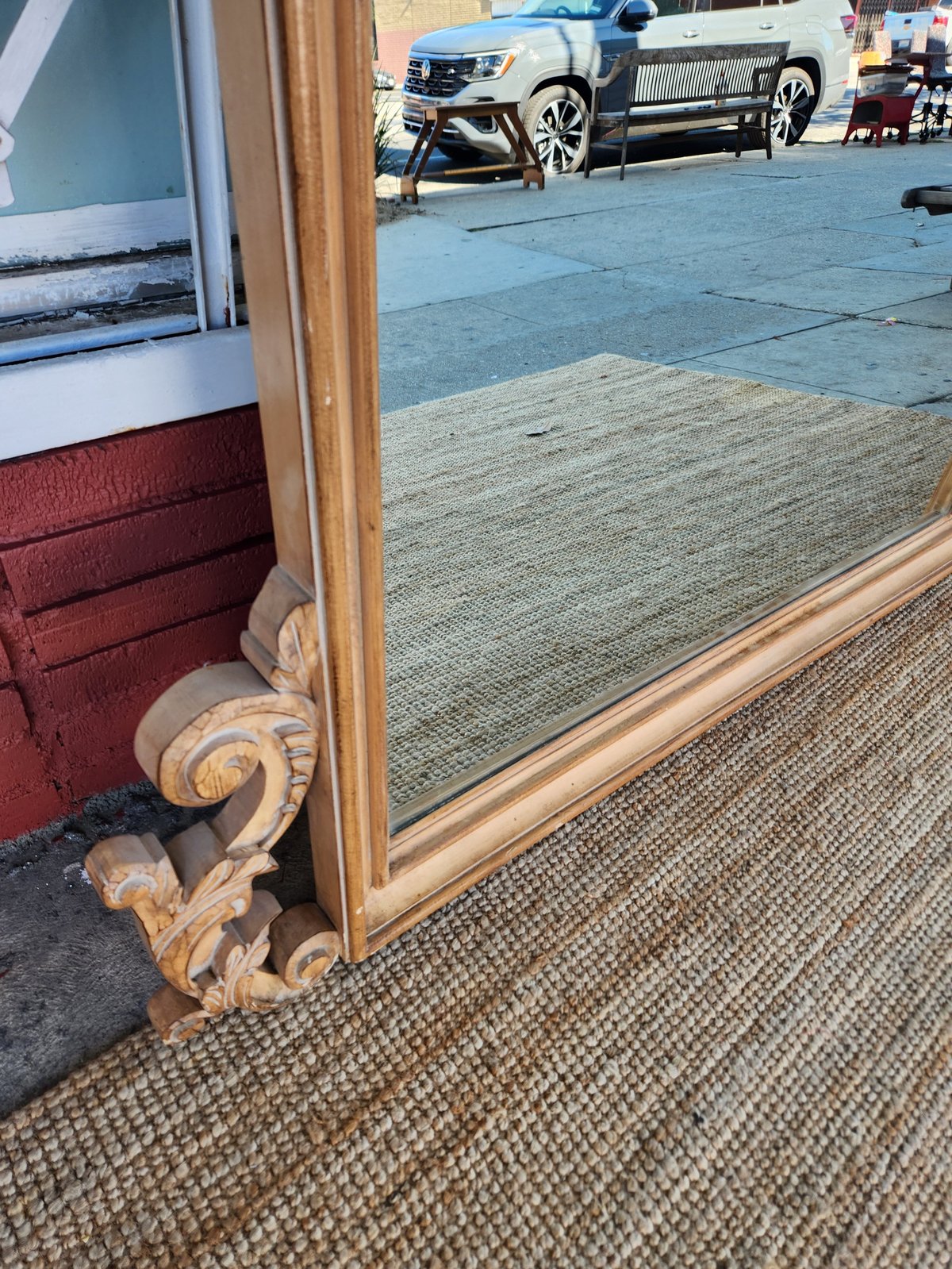 Mirror with ornate wooden frame leaning against interior wall, reflecting parked trucks outside