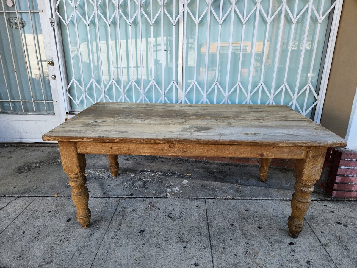Weathered wooden table with turned legs on a concrete sidewalk in front of a metal gate
