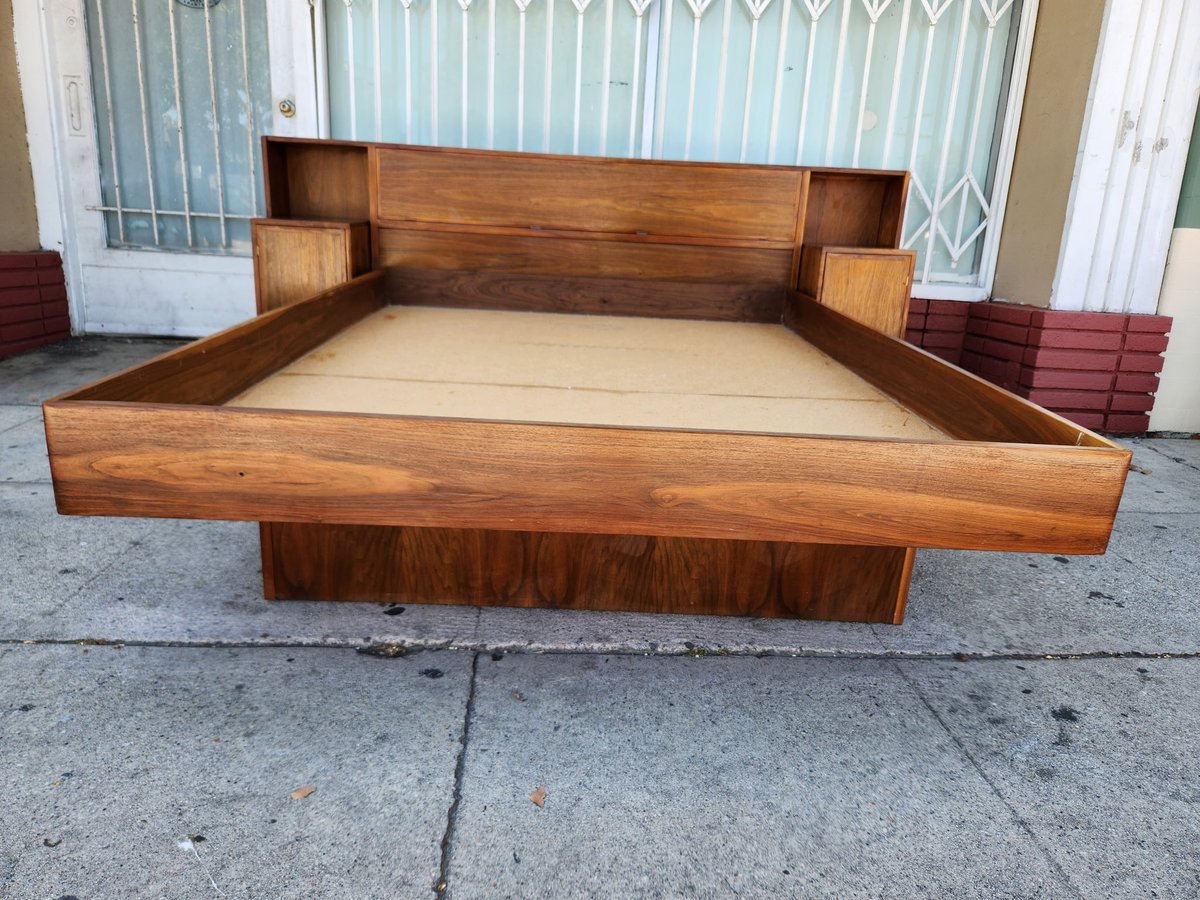 Mid-century modern wooden platform bed with attached side tables and cream-colored mattress on pavement