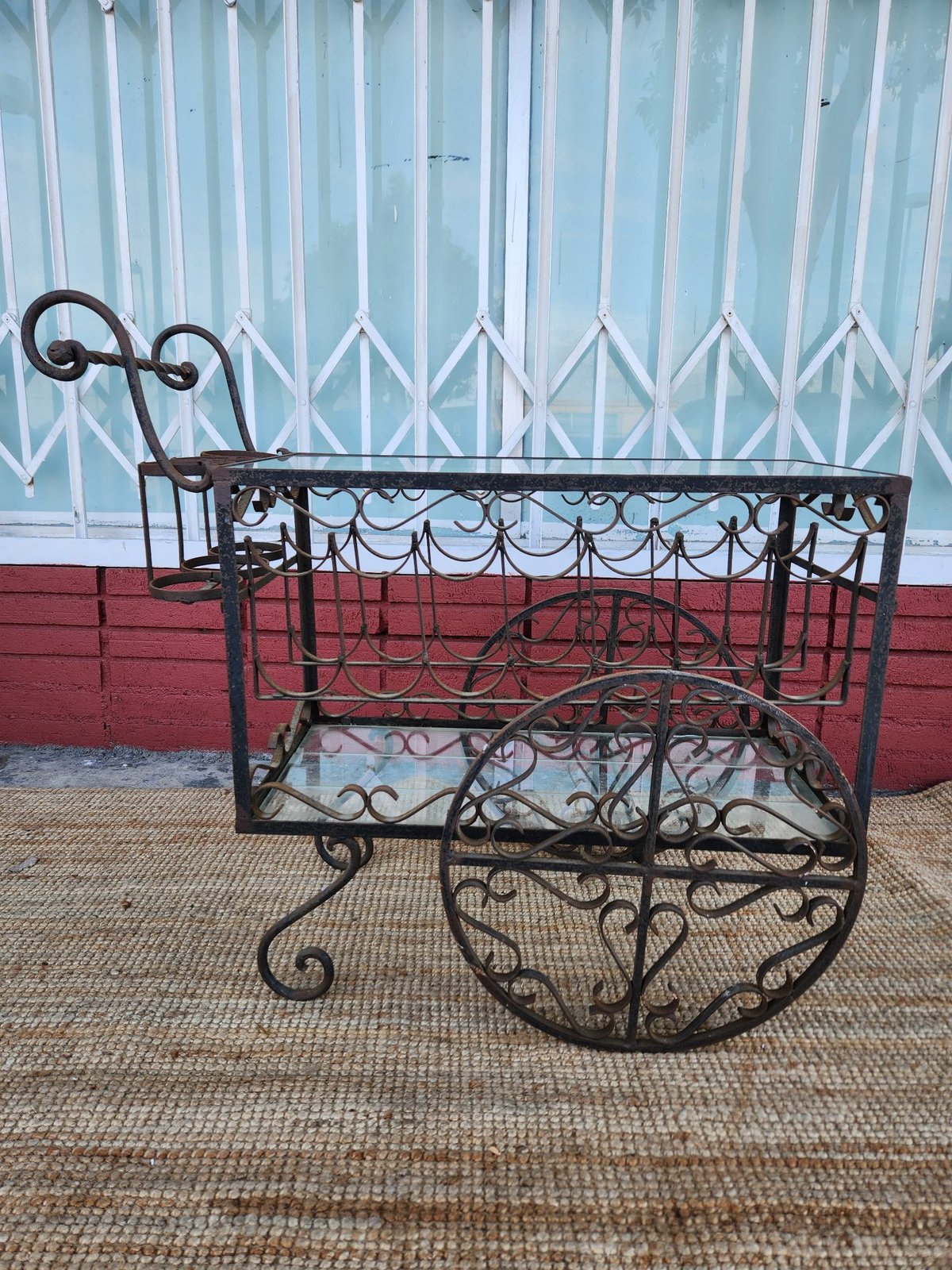 Ornate wrought iron plant cart with decorative scrollwork against a turquoise and red building backdrop
