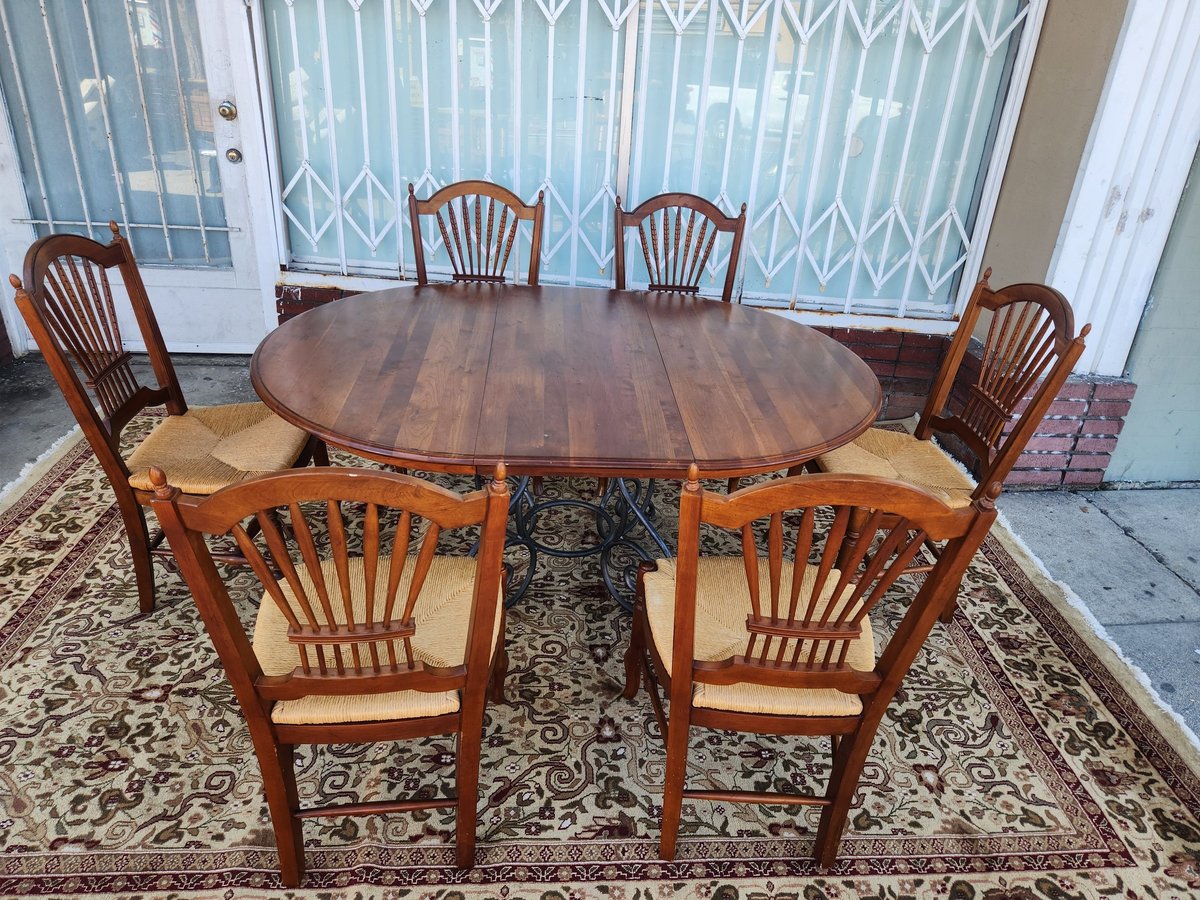 Oval wooden dining table with six wheat back chairs arranged on an ornate area rug