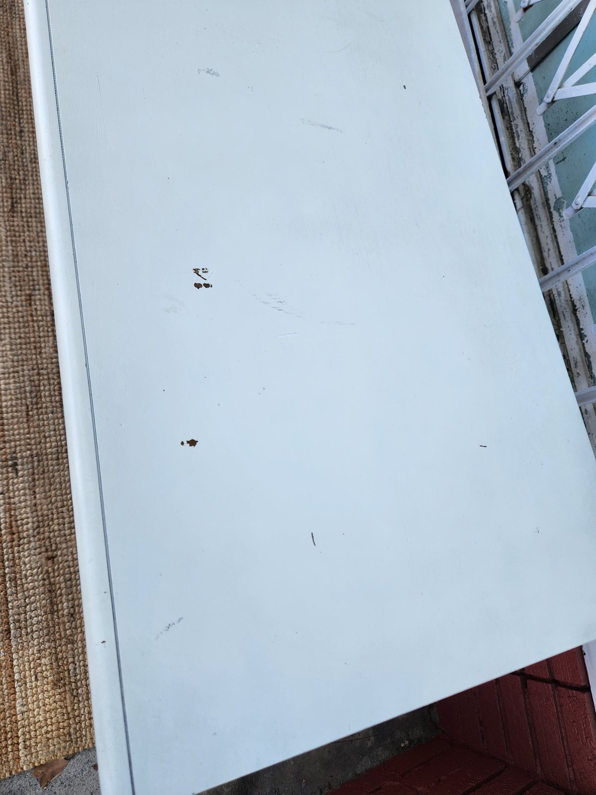 White ceiling or panel with scattered debris marks, brick wall on left, window frame on right, red surface at bottom