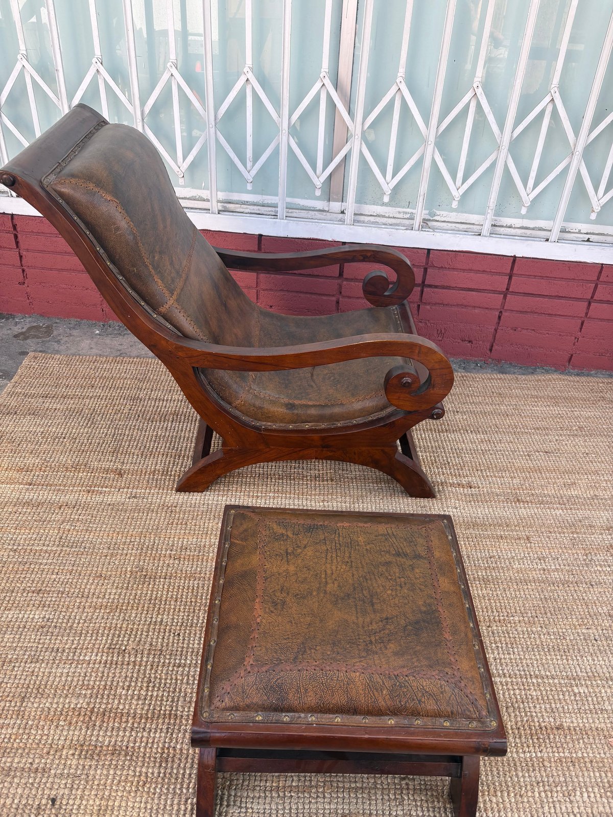 Vintage leather wingback chair with matching ottoman on patio, white gate and red brick wall in background
