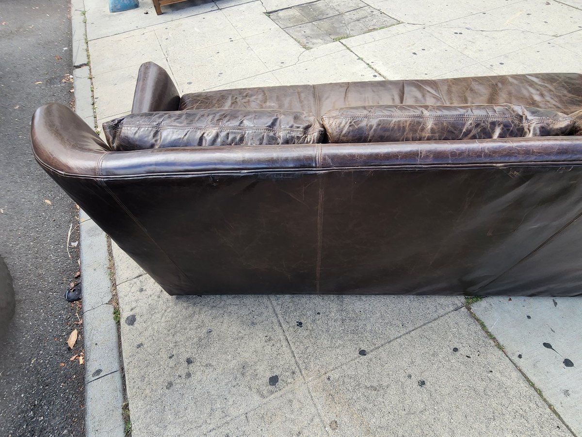 Brown leather sofa or couch lying on its back on a concrete sidewalk