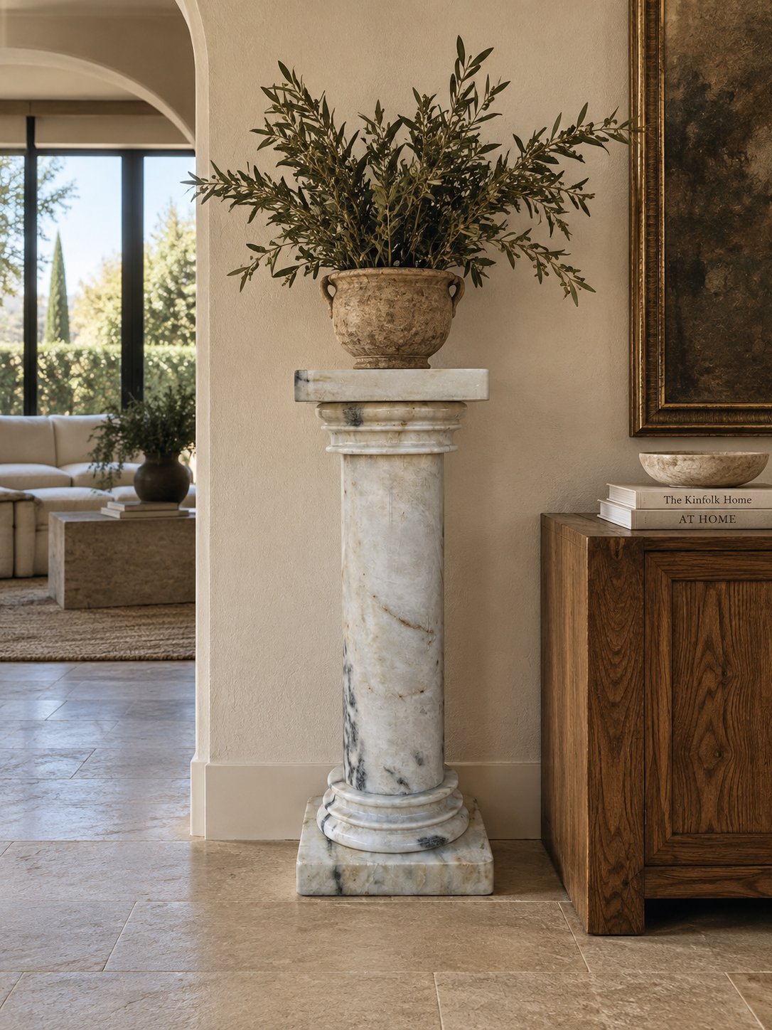 Marble pedestal with woven basket of dried greenery in elegant entryway with arched doorway and wood cabinet