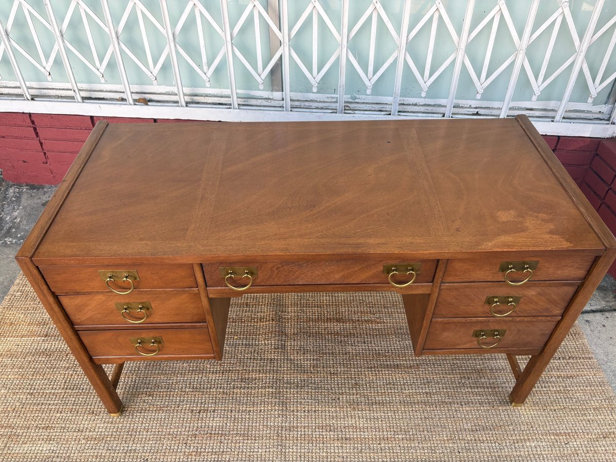 Vintage wooden desk with multiple drawers and brass handles on a beige area rug