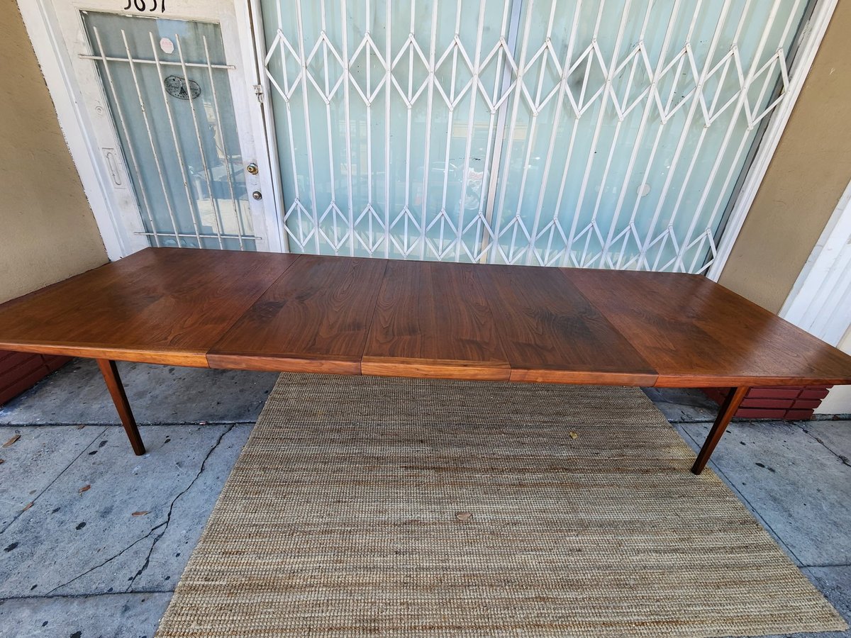 Mid-century modern wooden dining table with tapered legs on concrete patio, security gate behind
