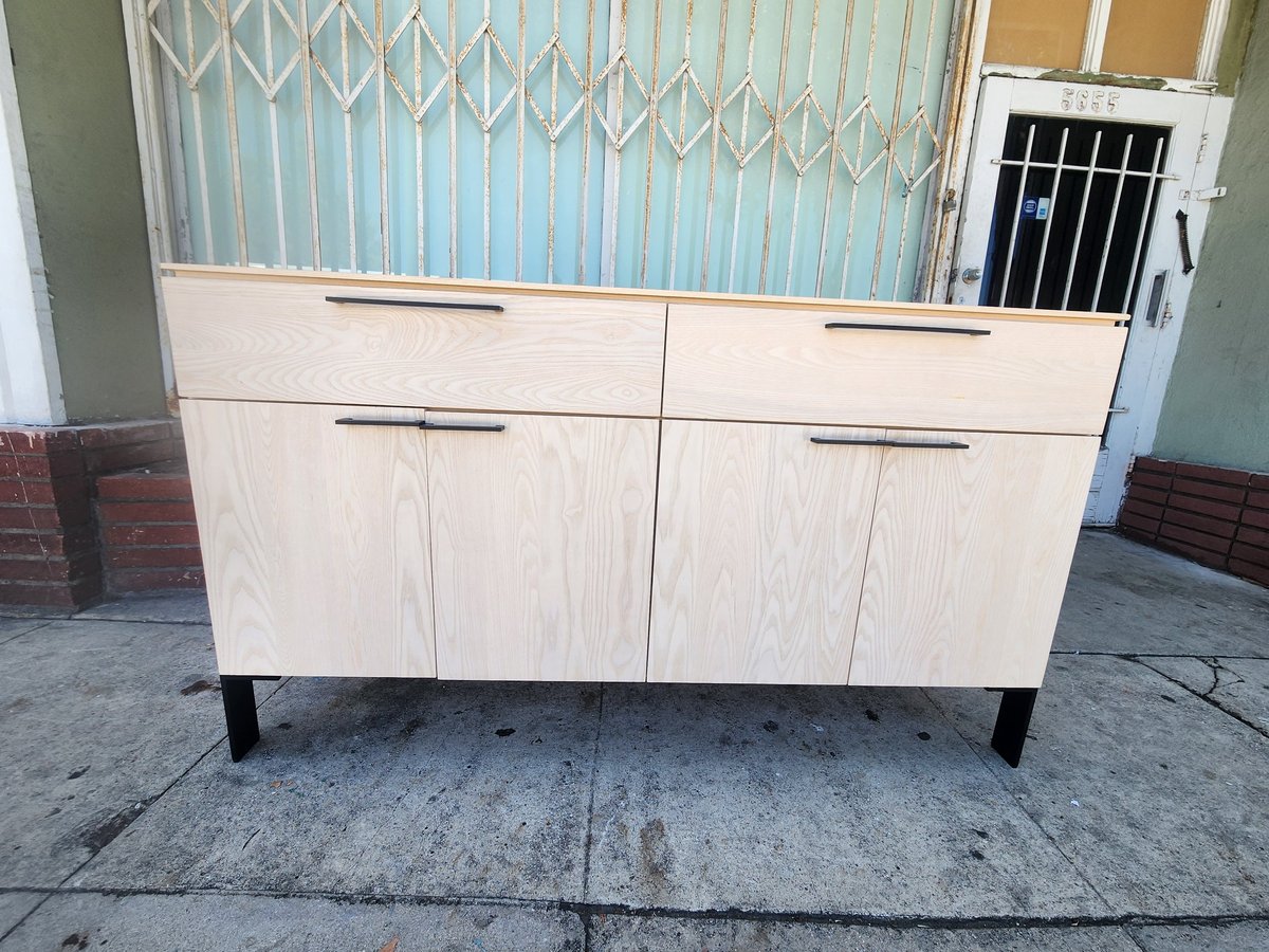 Light wood cabinet with four drawers and metal handles on concrete ground against corrugated metal background