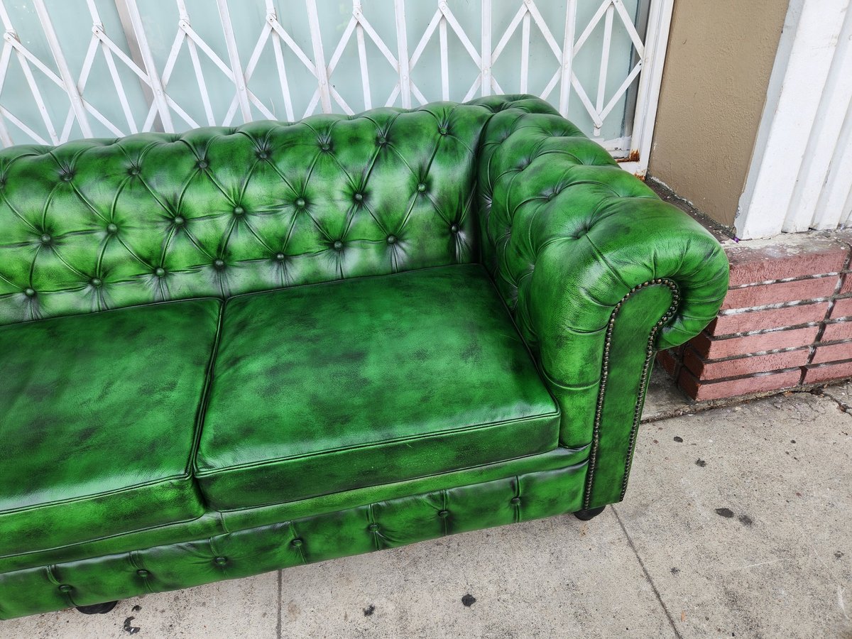Bright green leather Chesterfield sofa with tufted back and rolled arms, positioned on a sidewalk against a geometric patterned wall