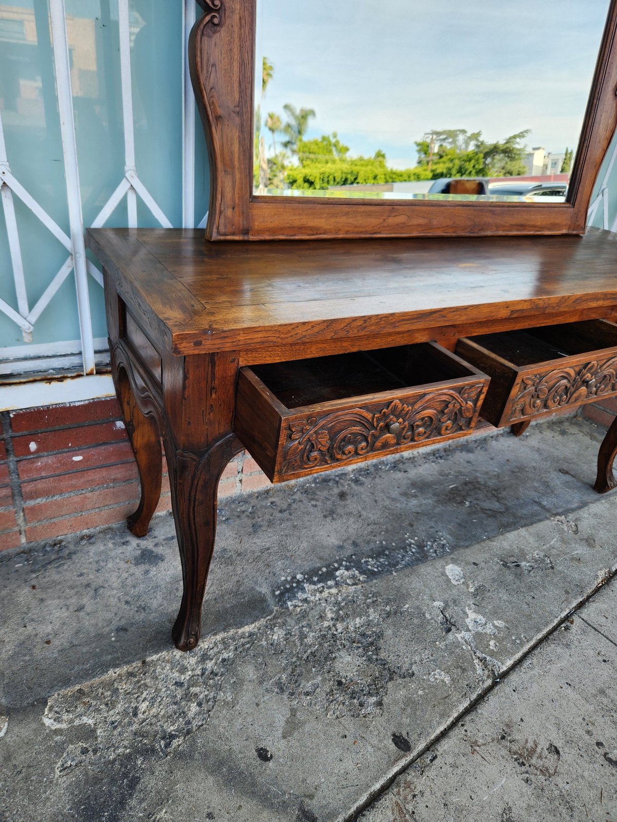 Wooden vintage console table with carved drawers on outdoor patio, lake view visible through window