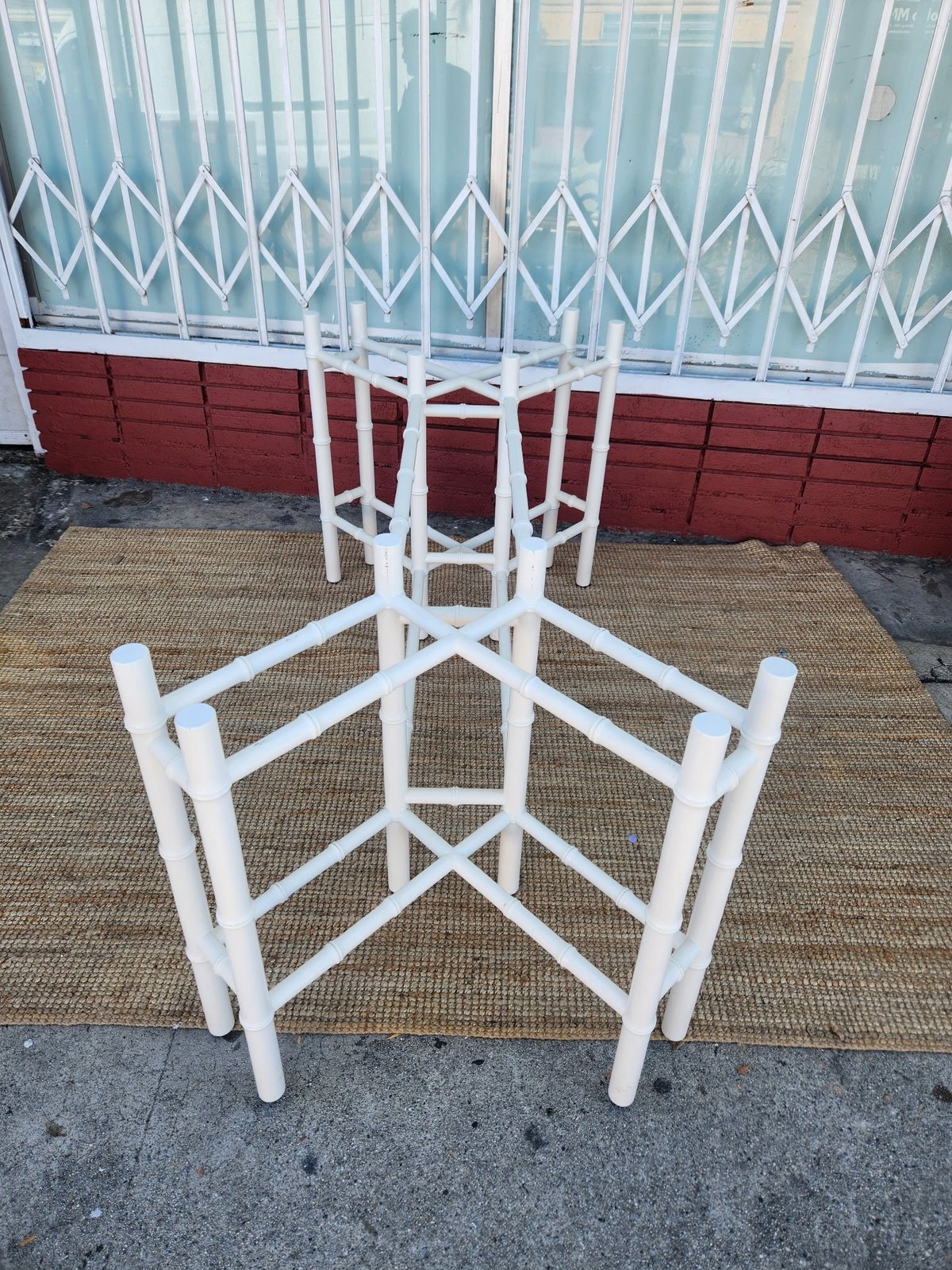 White metal clothing rack with geometric lattice frame displayed on pavement against red metal storefront