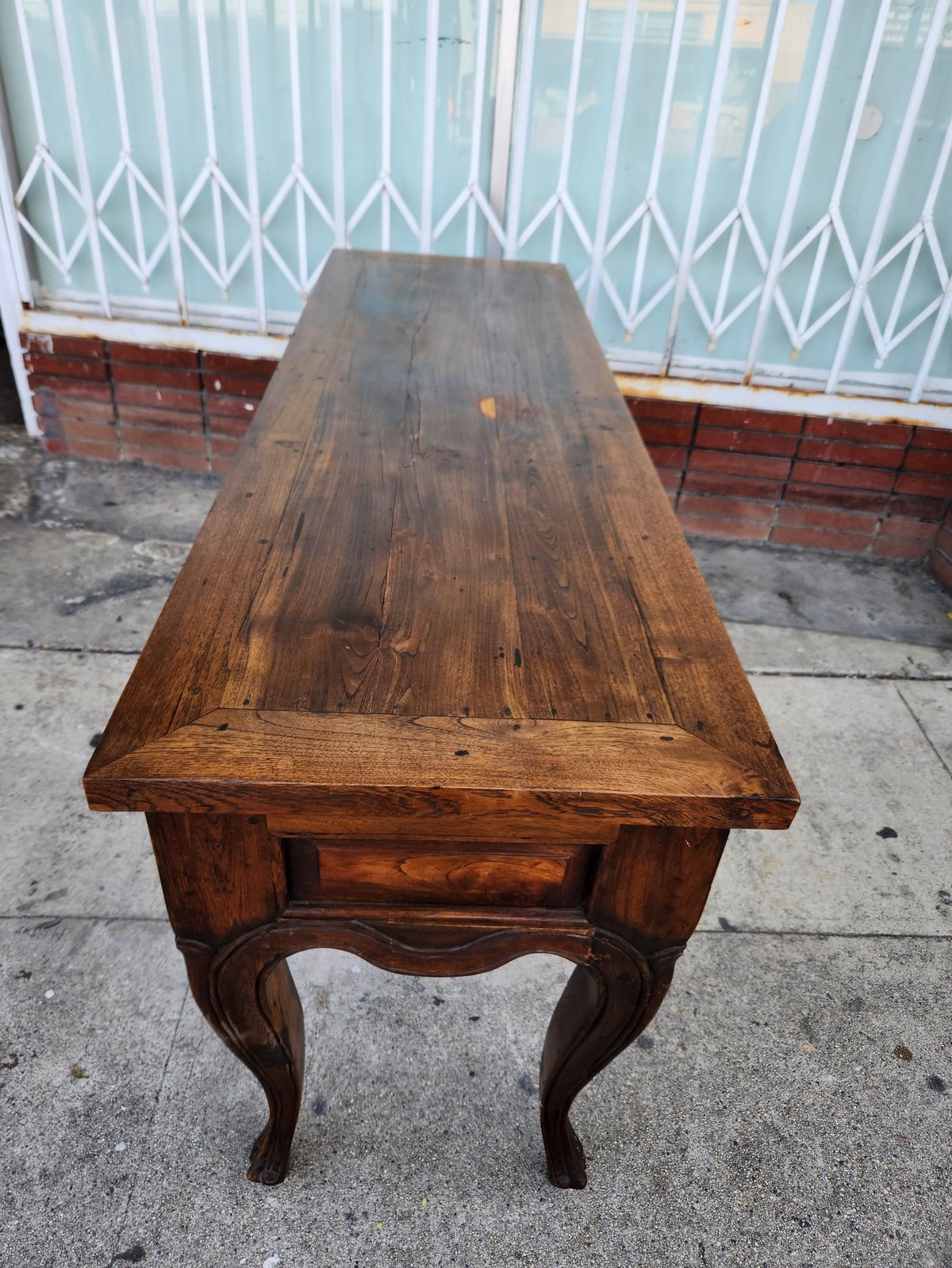 Antique wooden table with curved legs on a concrete surface against a metal gate backdrop
