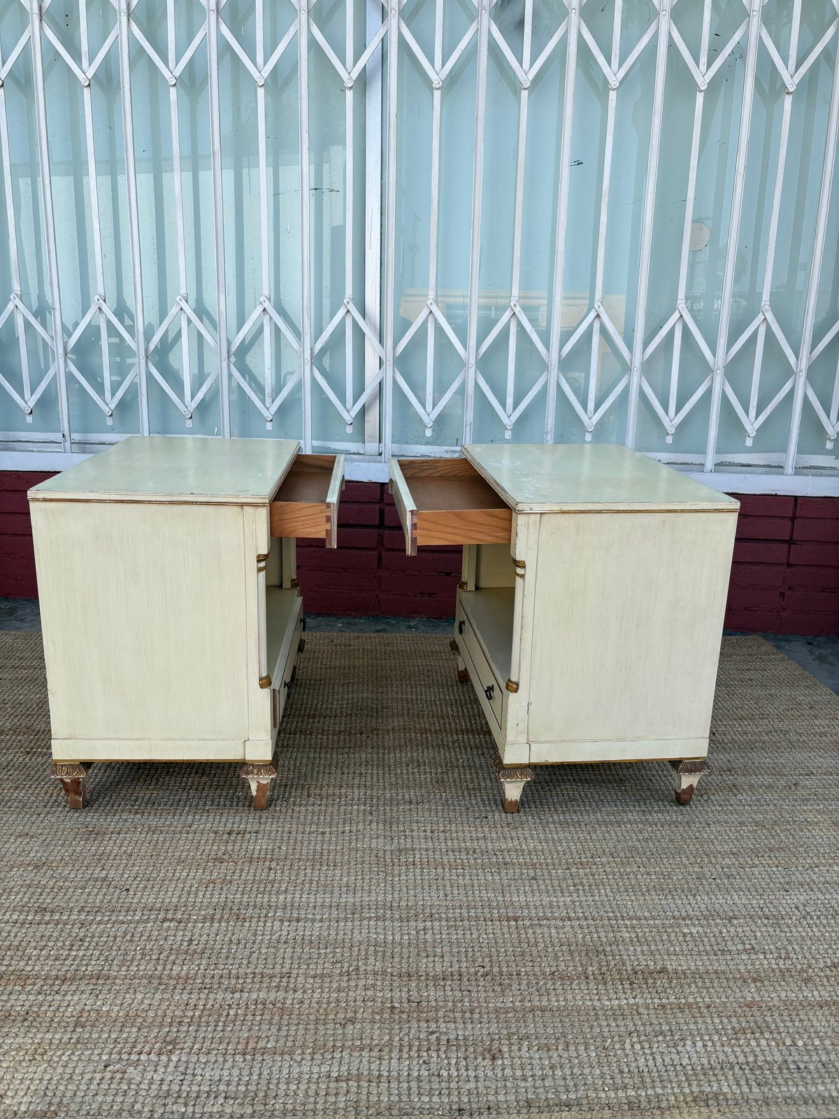 Two cream-colored wooden desks with open drawers connected by a brown center section on a gray concrete floor.