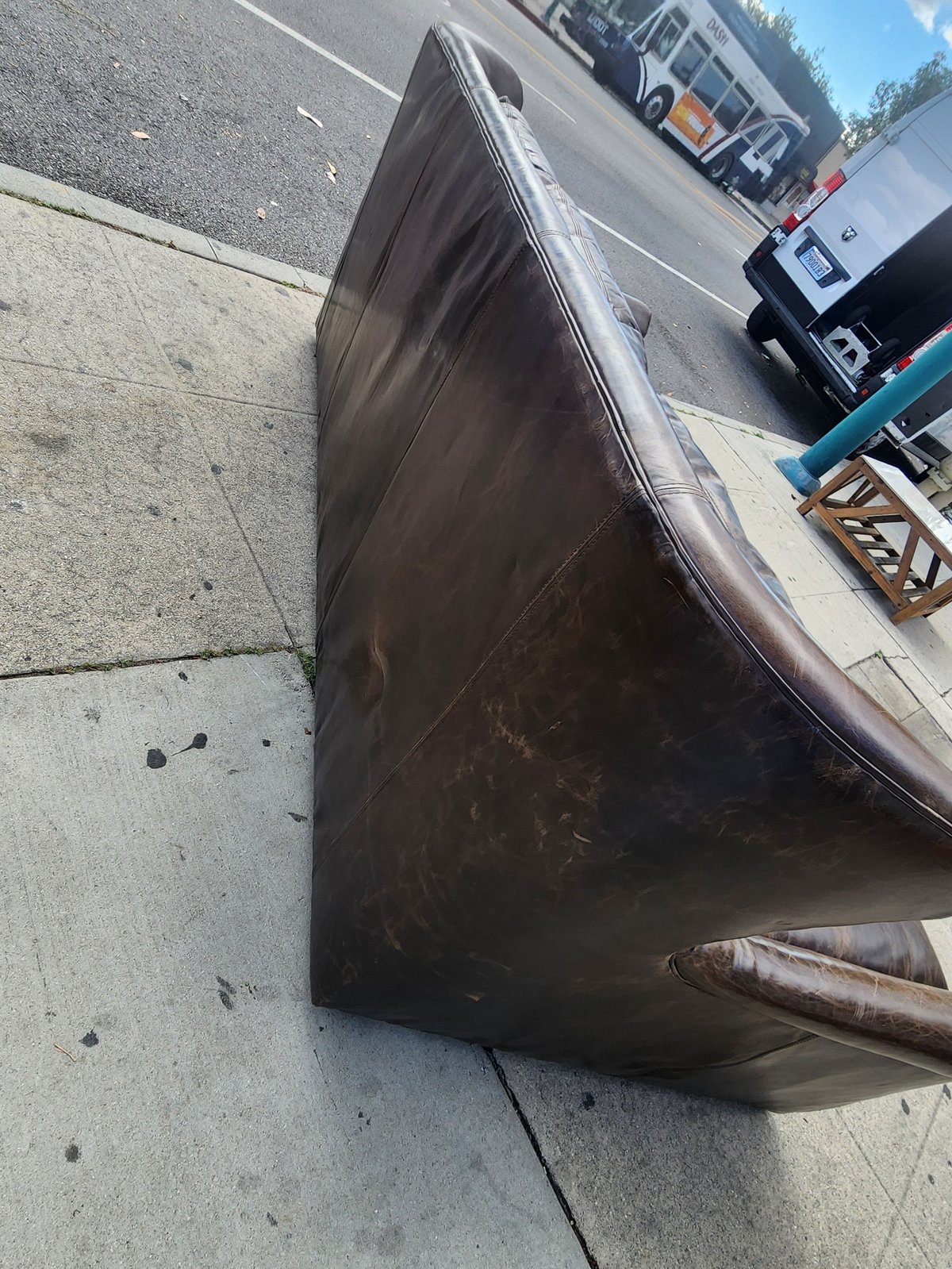 Dark vehicle door lying on concrete pavement in parking lot with trucks visible in background