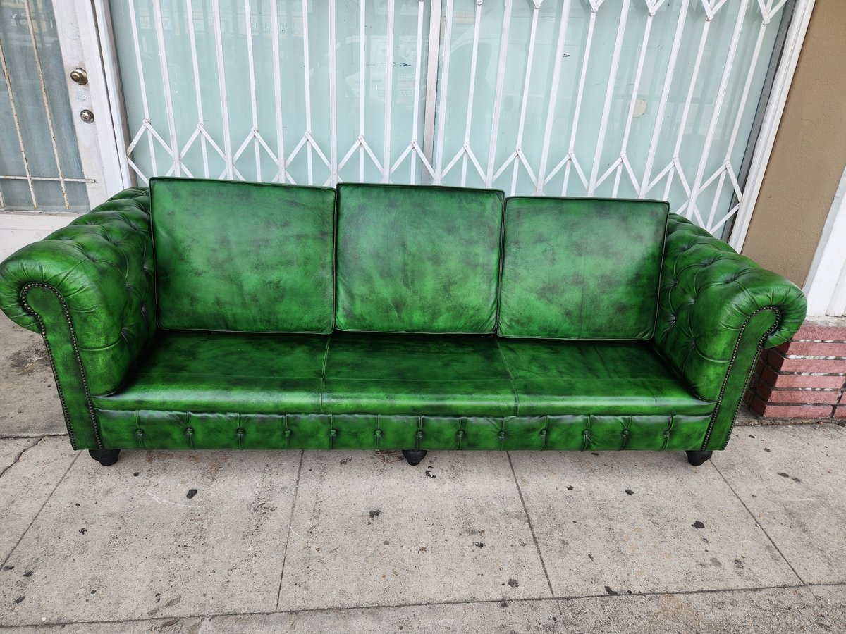 Green Chesterfield sofa with rolled arms on a concrete sidewalk in front of white shuttered doors