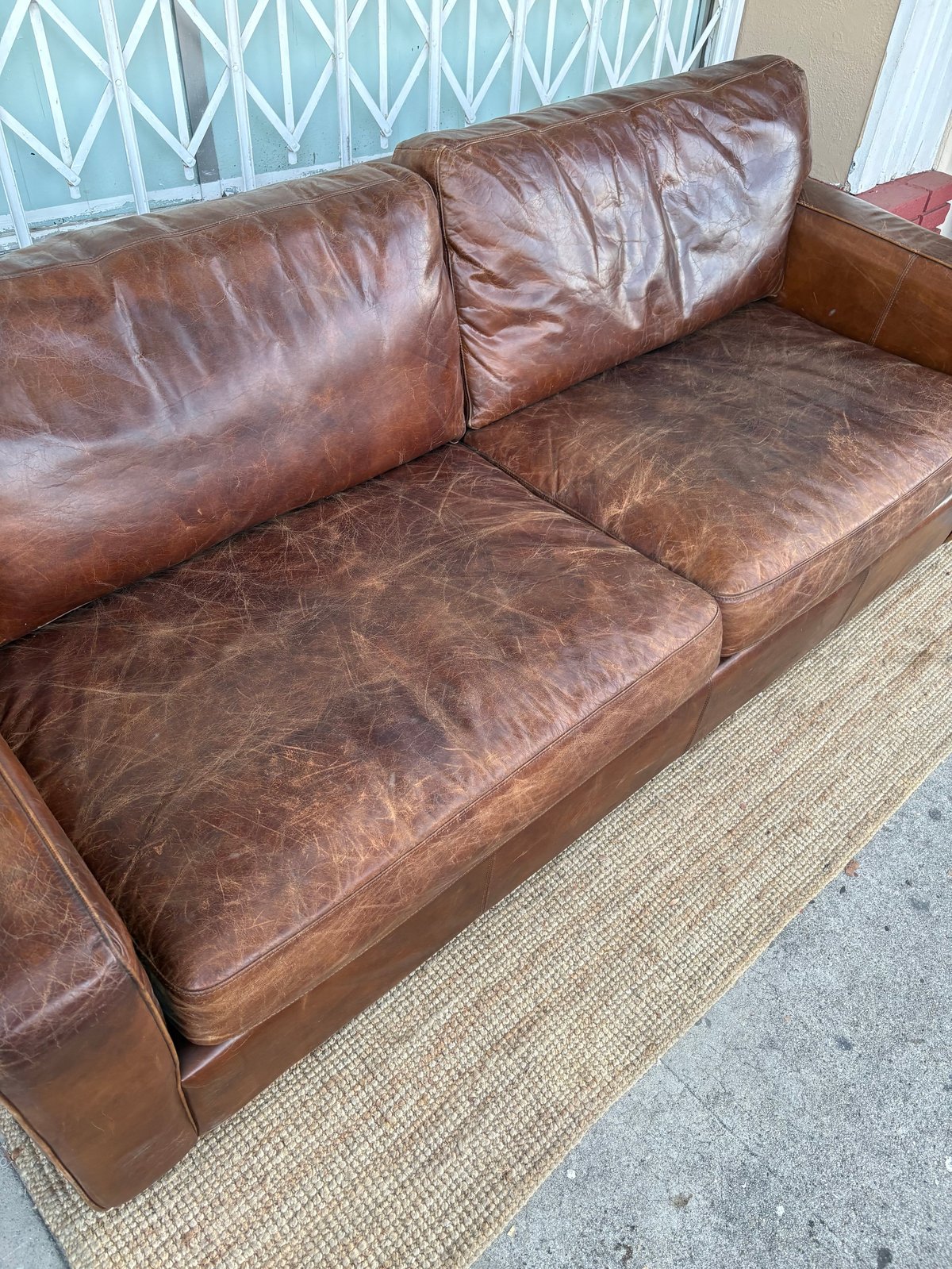 Brown leather sofa with wooden frame on beige rug, showing wear and patina