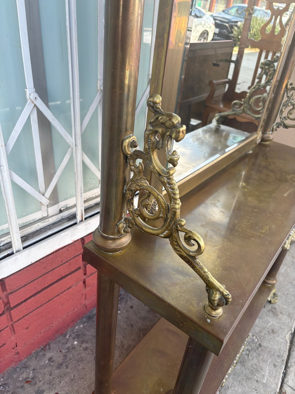 Ornate brass fireplace andiron with decorative scrollwork displayed on wooden shelf in antique store