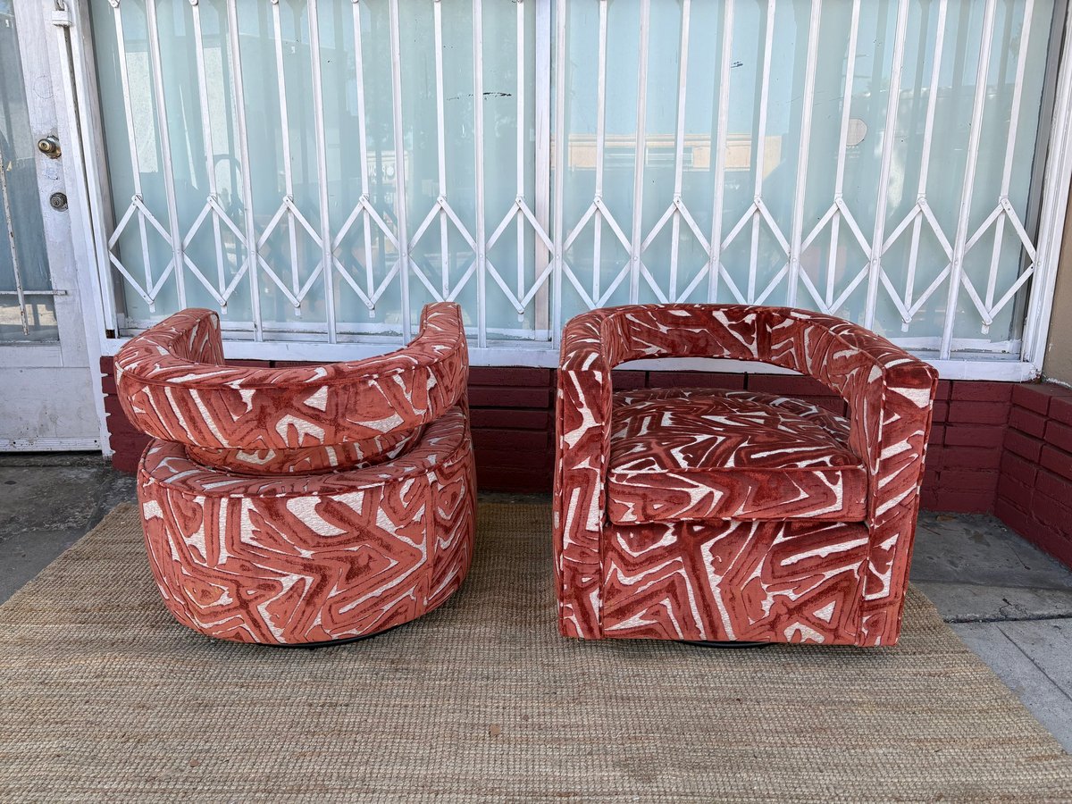 Two red patterned armchairs facing each other on a beige rug in front of white metal folding gates and striped windows