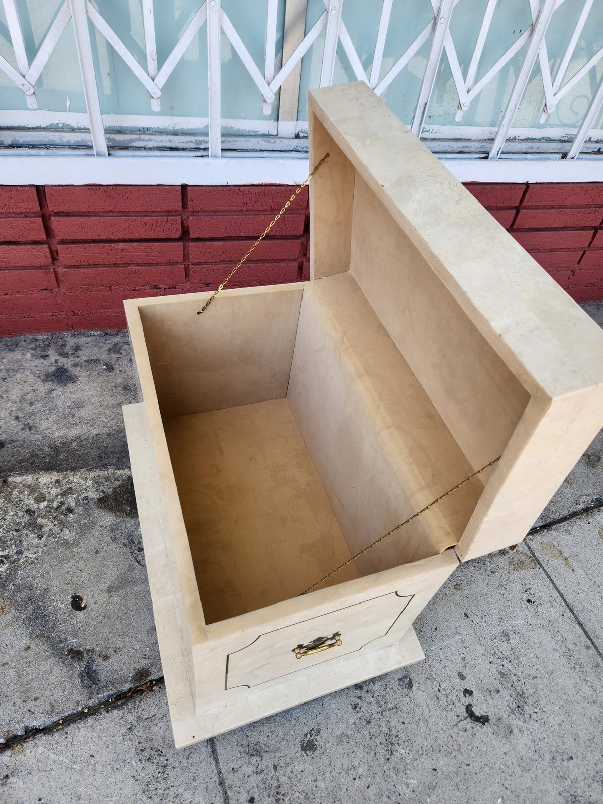 Open wooden box or crate with divided interior sections on concrete ground near red and white fencing