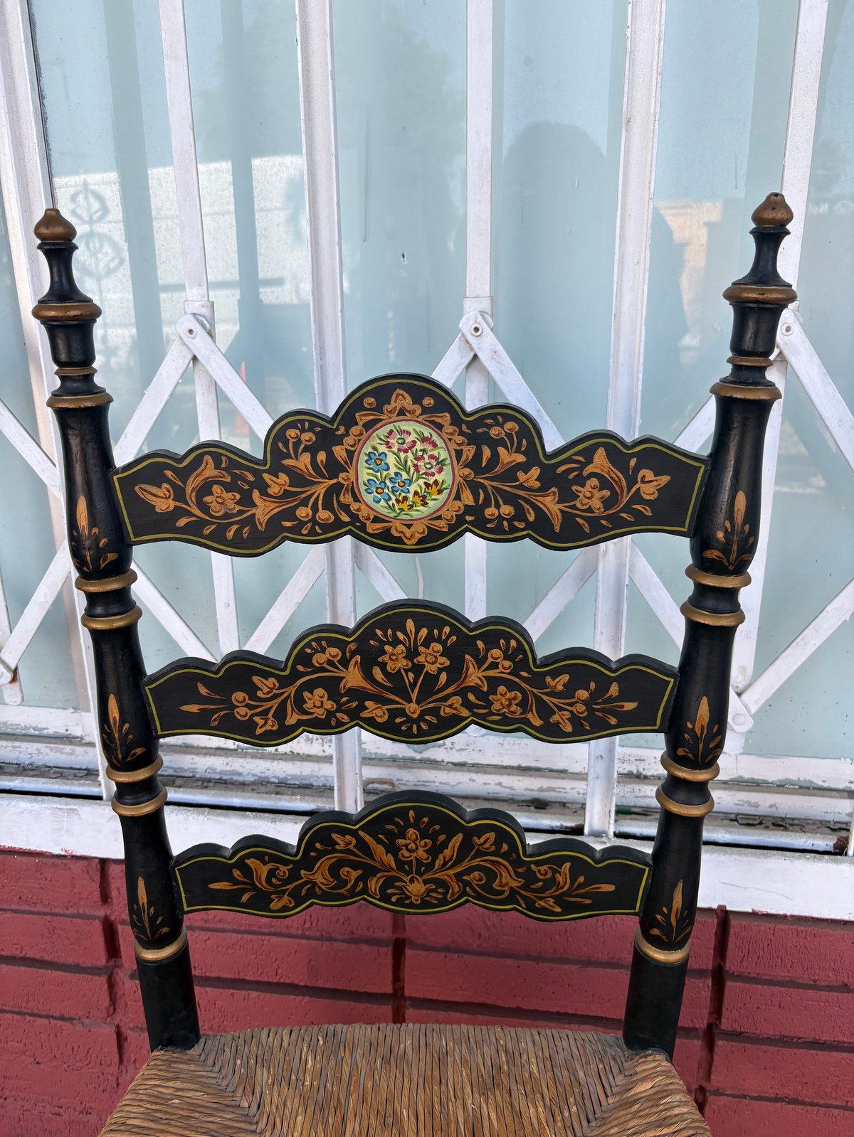 Black wooden chair with ornate gold floral inlay and decorative finials displayed against a window
