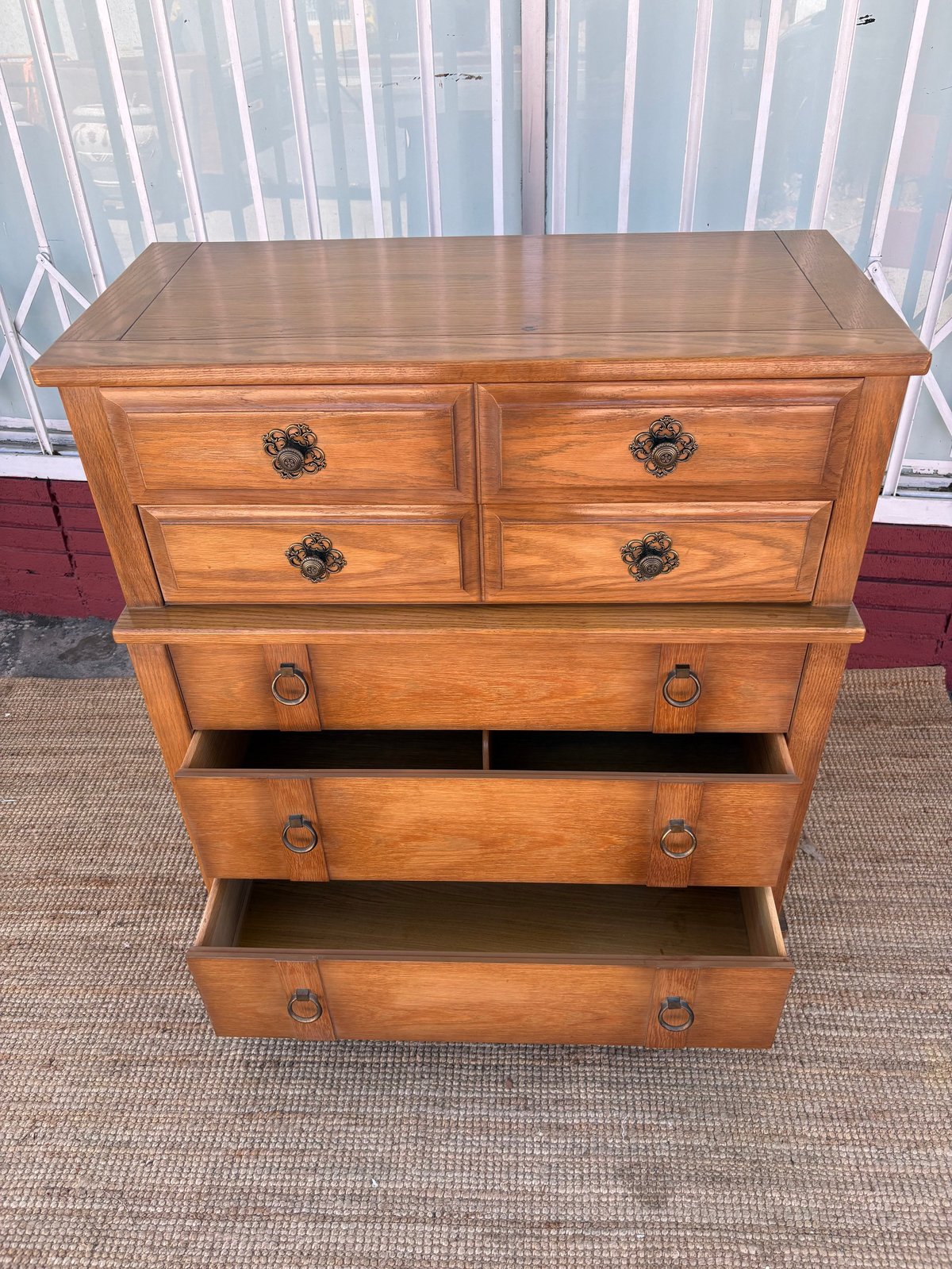 Wooden dresser with five drawers and metal handles on a carpet with windows in background