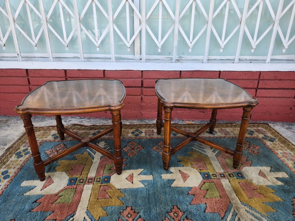 Two wooden side tables with glass tops on a colorful patterned rug against a red brick wall.