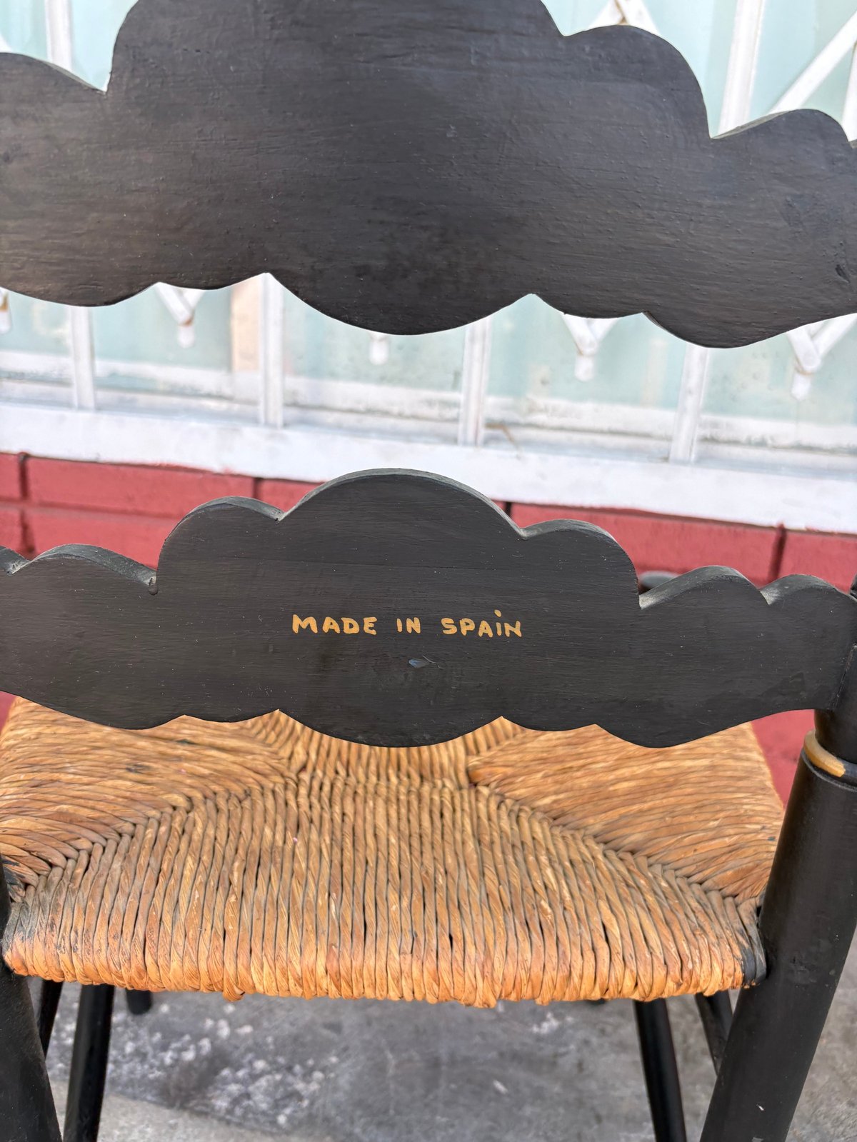 Black wooden chair with wavy cloud-shaped backrest and woven rush seat marked Made in Spain