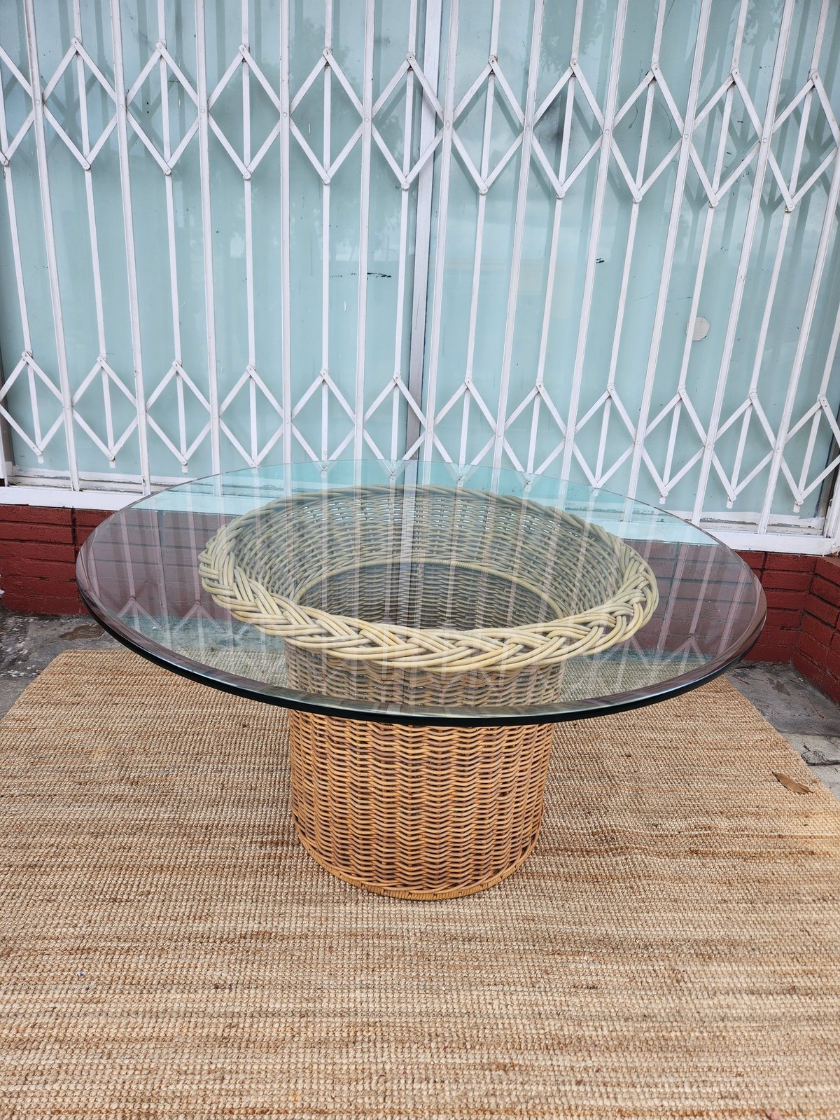 Round glass-top dining table with woven wicker basket base on outdoor patio