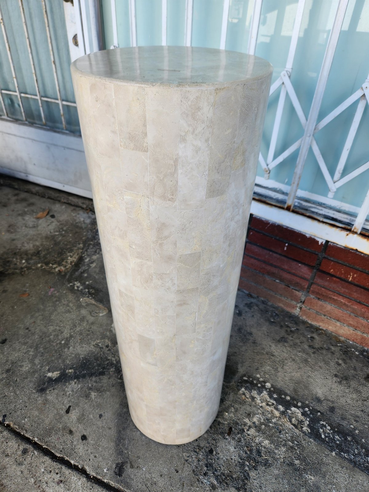 Tall white cylindrical concrete or stone column standing on concrete ground outside a building