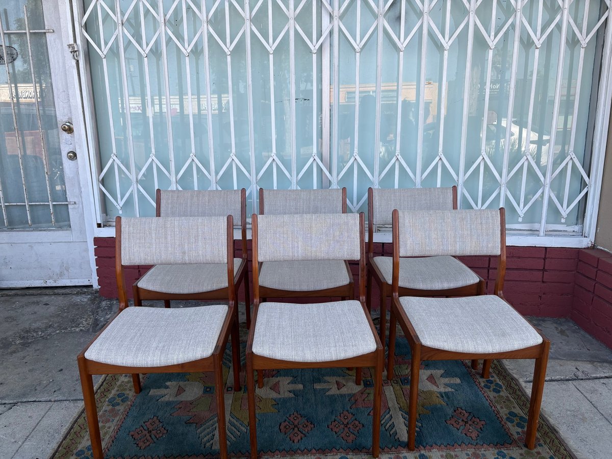 Three wooden dining chairs with light gray upholstered seats arranged on a patterned rug in front of a metal accordion gate.
