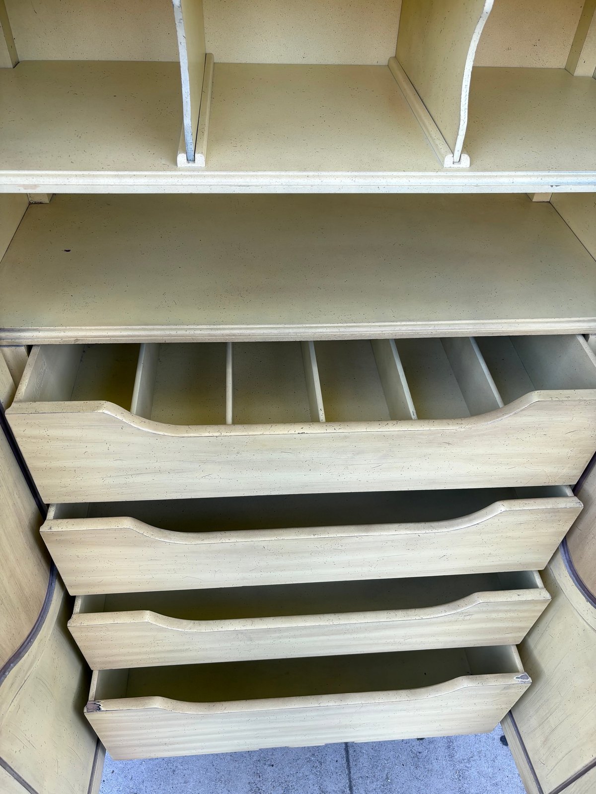 Open wooden dresser drawers with dividers and compartments inside a white shelving unit