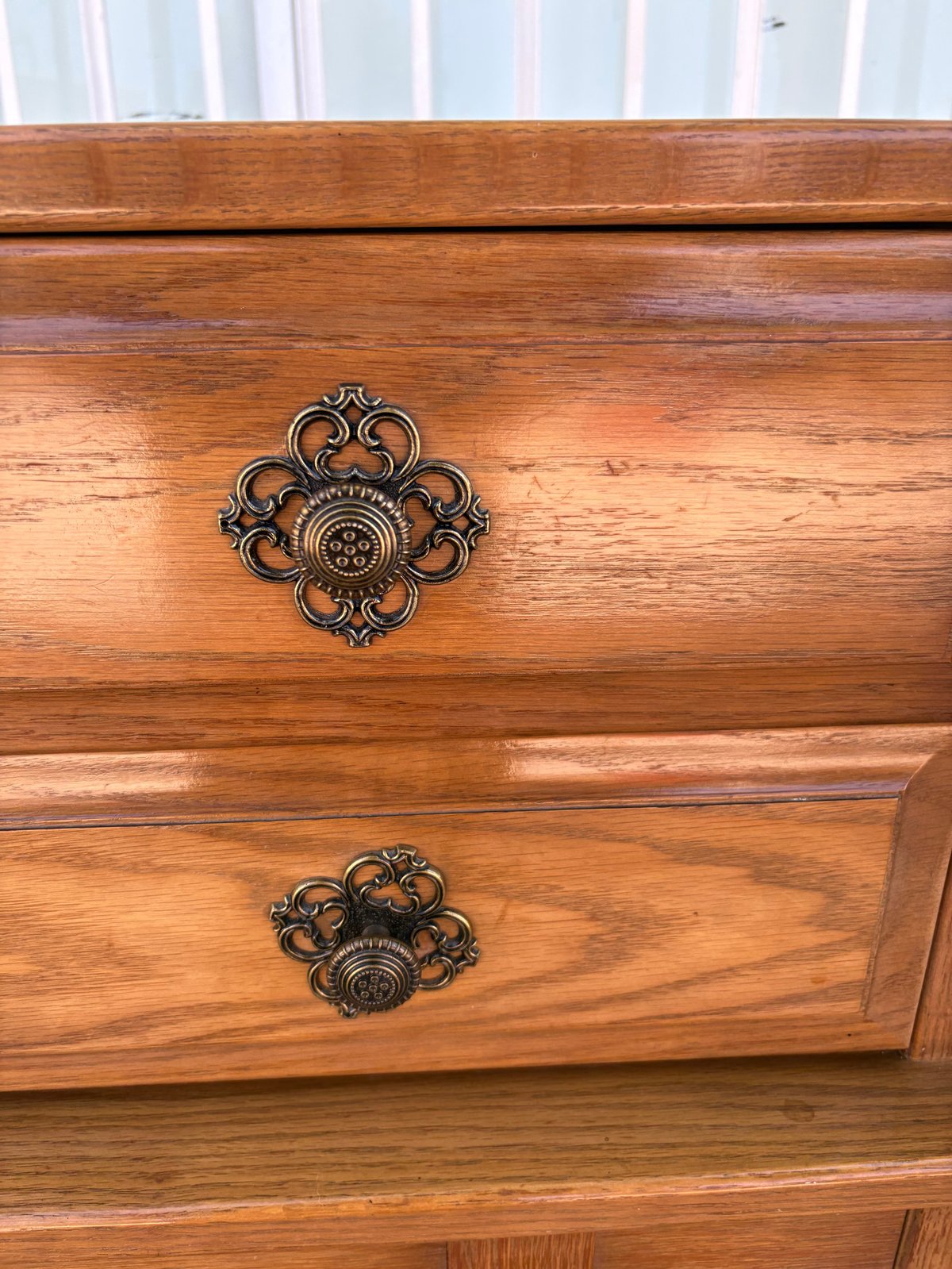 Wooden dresser drawers with ornate bronze decorative drawer pulls against a window