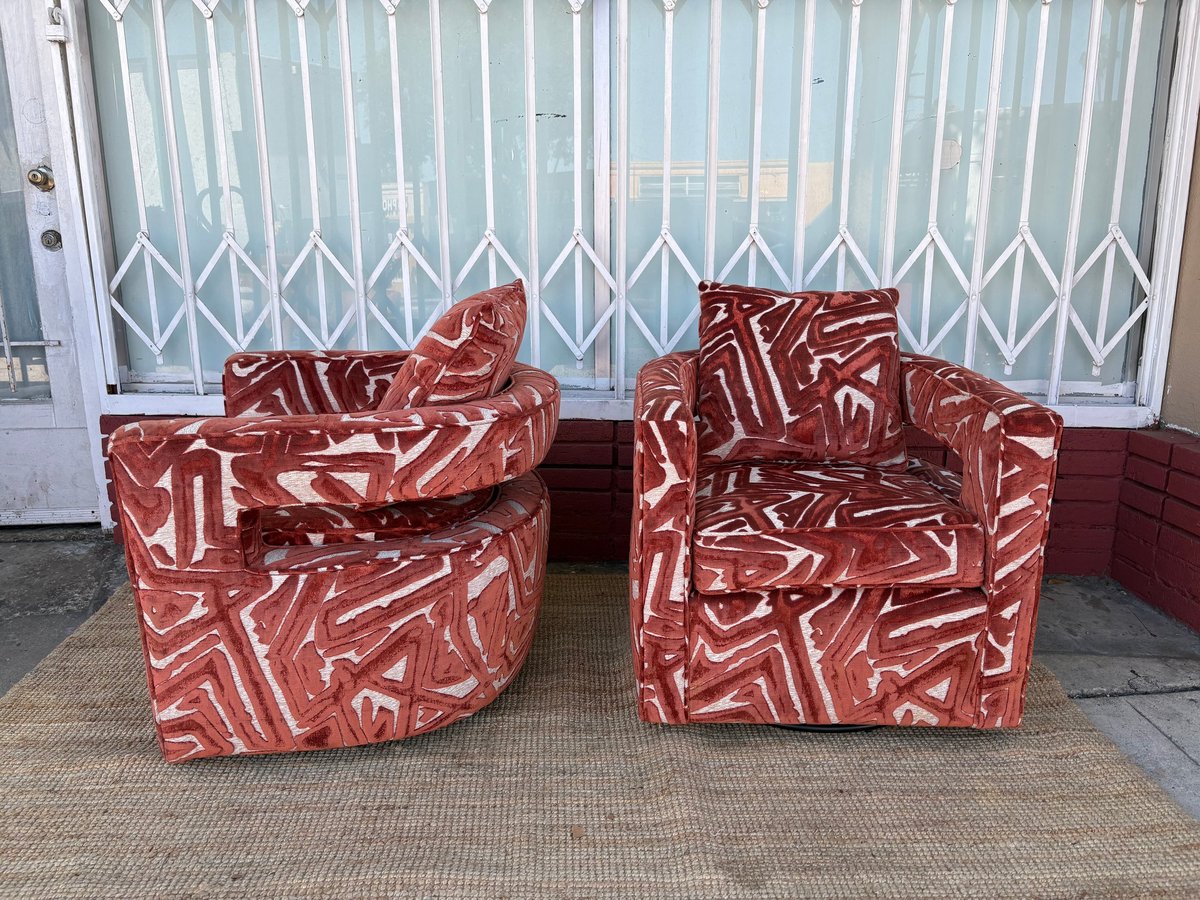 Two red patterned armchairs with geometric design positioned in front of white vertical blinds and brick wall