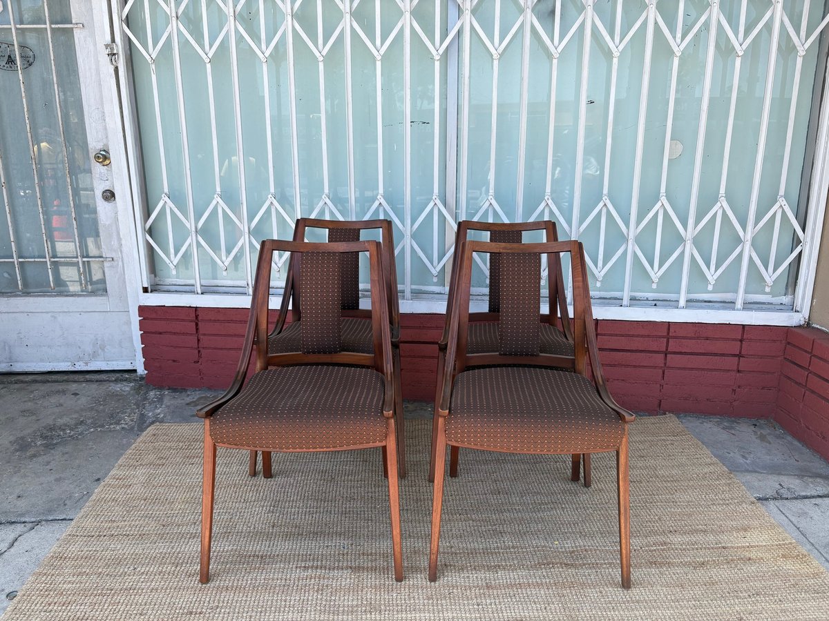 Two mid-century modern wooden chairs with woven seats on a beige rug against a storefront with metal security gate