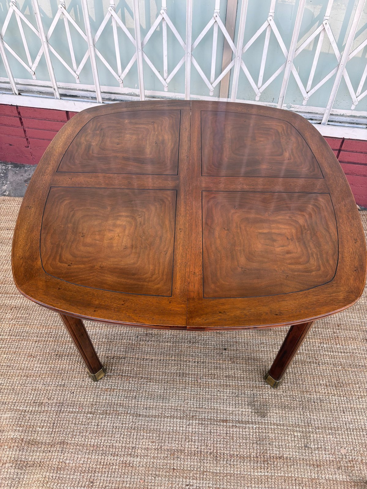 Wooden dining table with rounded corners and four-panel veneer top on wooden legs, photographed outdoors.