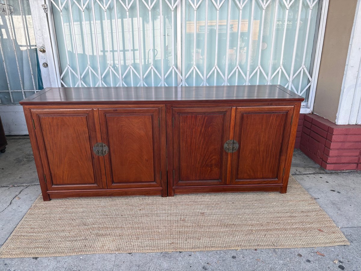 Large wooden cabinet with four doors on a woven beige rug outside a storefront with white metal gate