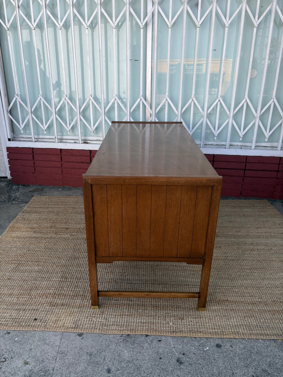 Mid-century wooden desk with metal top on beige rug against white security gate and red wall