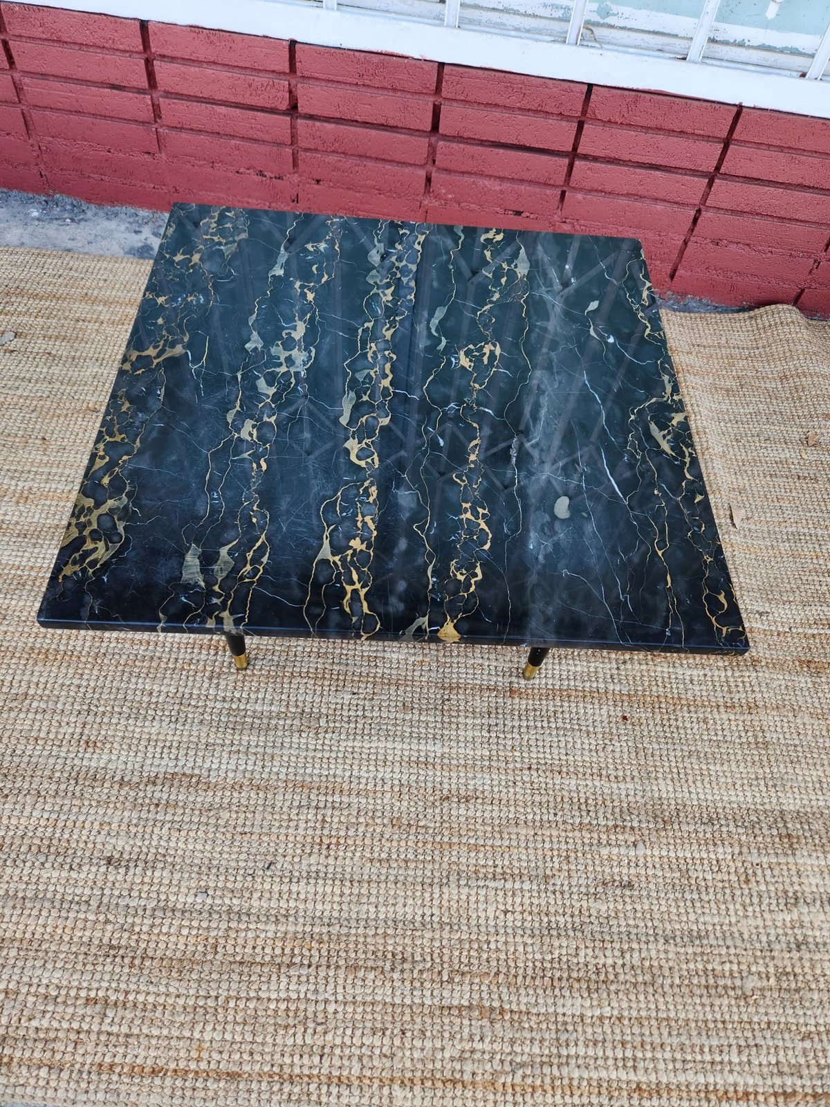Black marble-topped table with gold veining on concrete surface against red fence